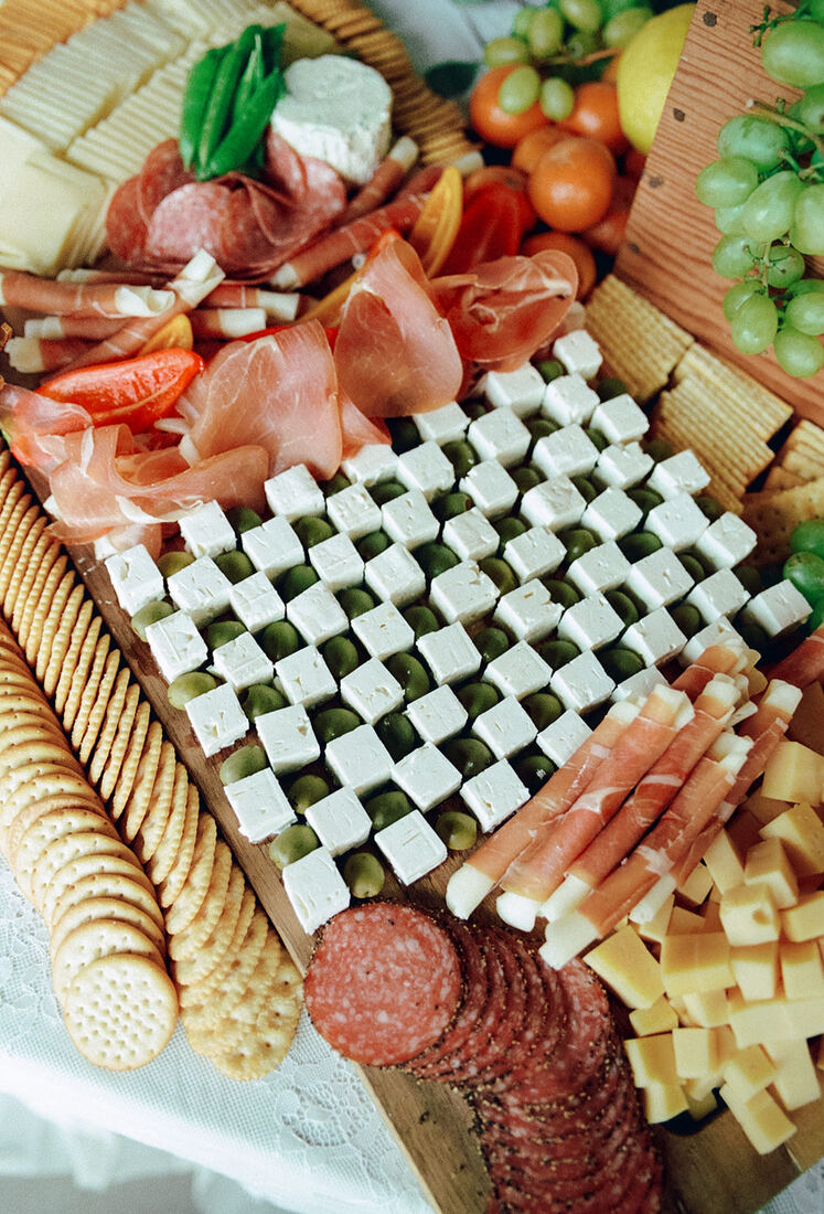 Detail of a grazing board with feta and olives arranged in a checkerboard pattern beside prosciutto
