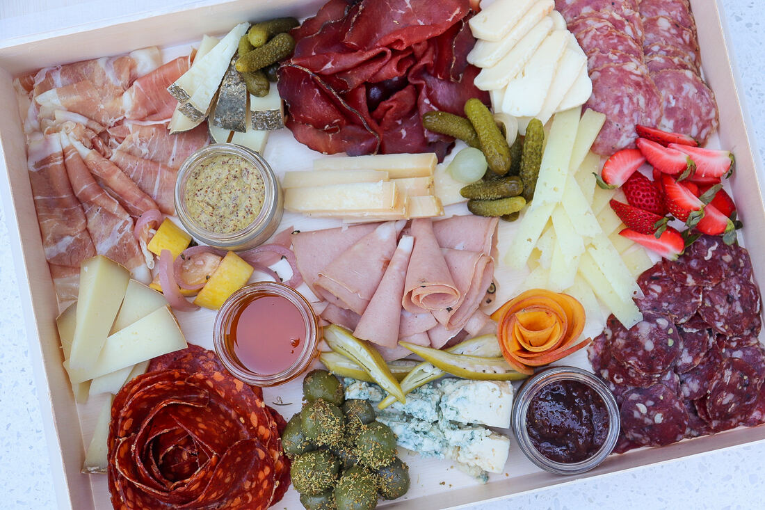 Overhead of a large grazing platter with prosciutto, salami roses, cheeses, strawberries and house condiments